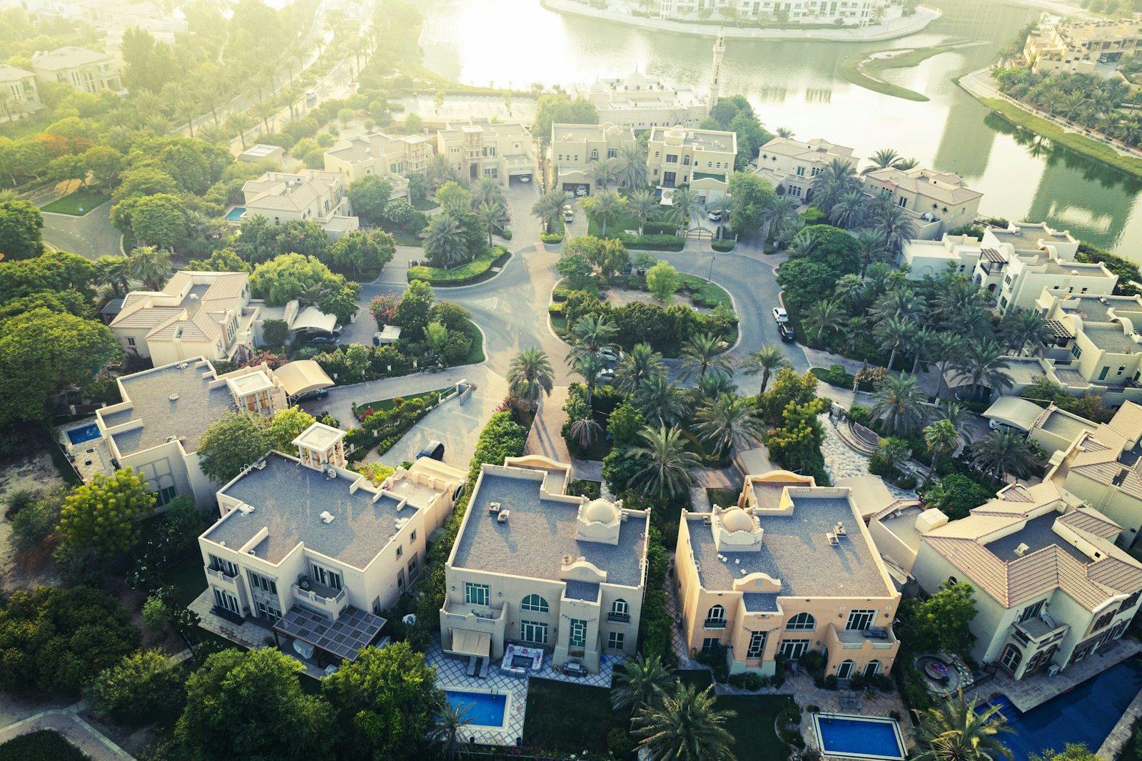 Aerial view of a mature Dubai villa community, large detached villas with private pools set among palms and curving landscaped streets.