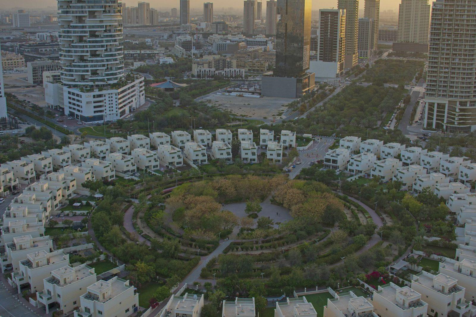 Aerial view of a Dubai townhouse community laid out around a circular landscaped park, low-rise apartment blocks and villas ringing the green.