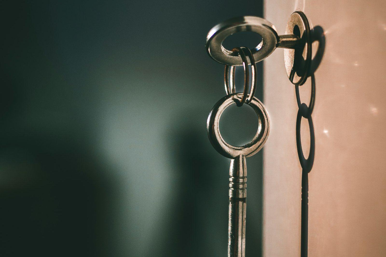 A set of keys left hanging in the lock of a door, lit from one side.