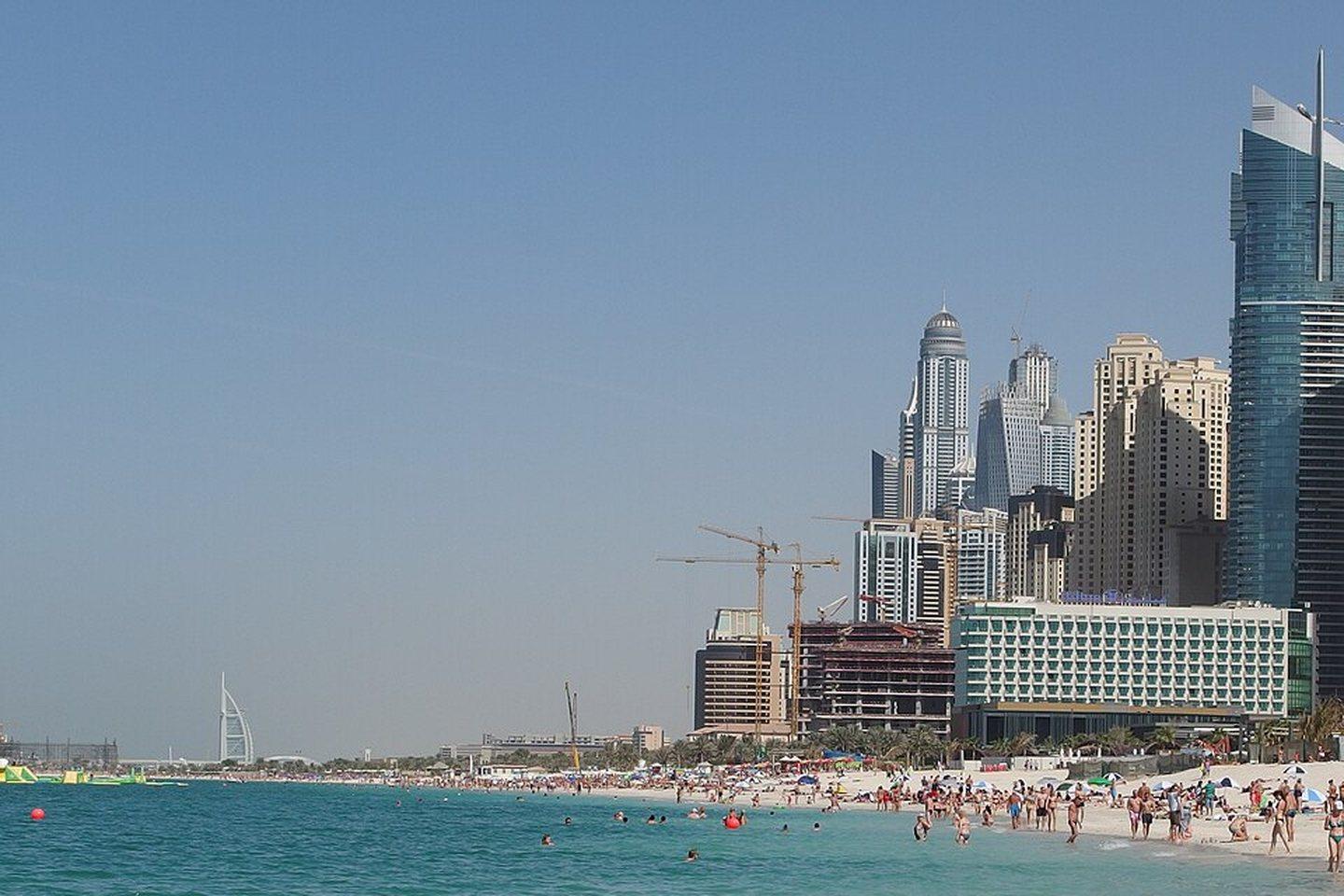 The Jumeirah Beach Residence coastline by day: turquoise shallows, the wide public beach and the JBR tower wall running along the shore.