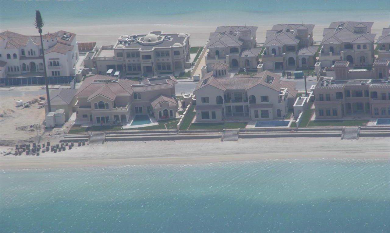 Beachfront villas along a Palm Jumeirah frond, each plot running from its private pool terrace down to the sand and the water of the frond channel.