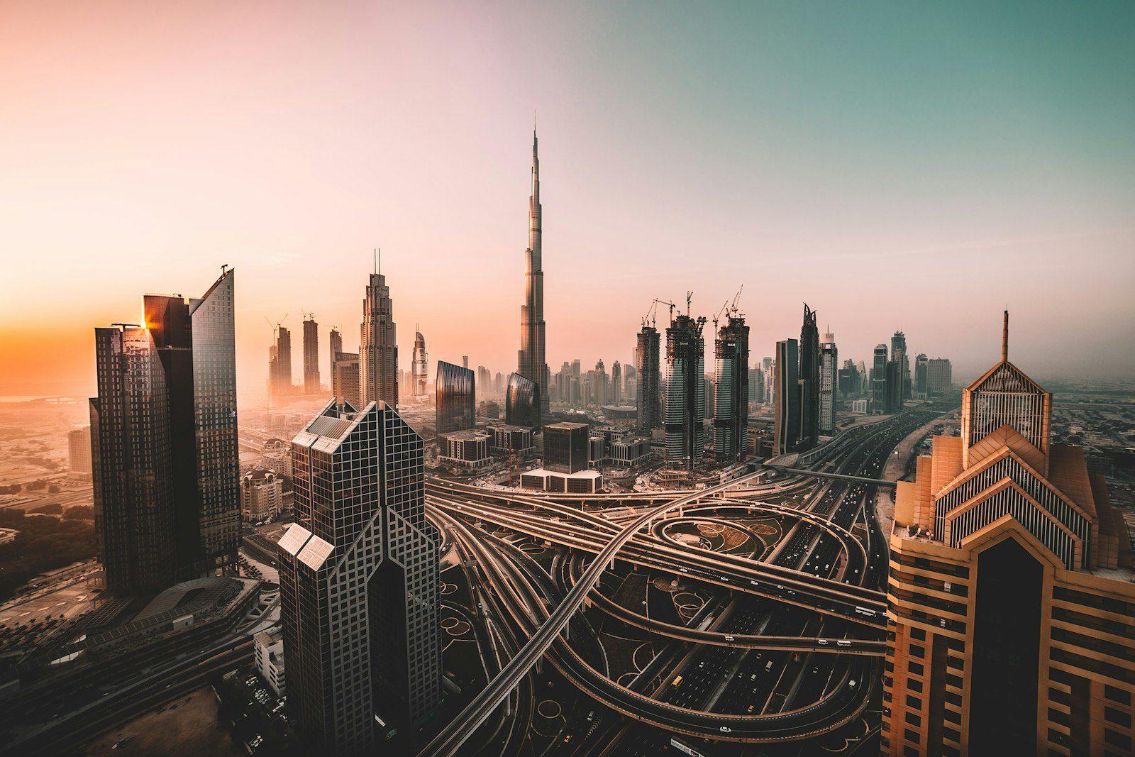Downtown Dubai at first light, the Burj Khalifa rising above the Sheikh Zayed Road interchange as its curving ramps loop between the high-rise cluster.